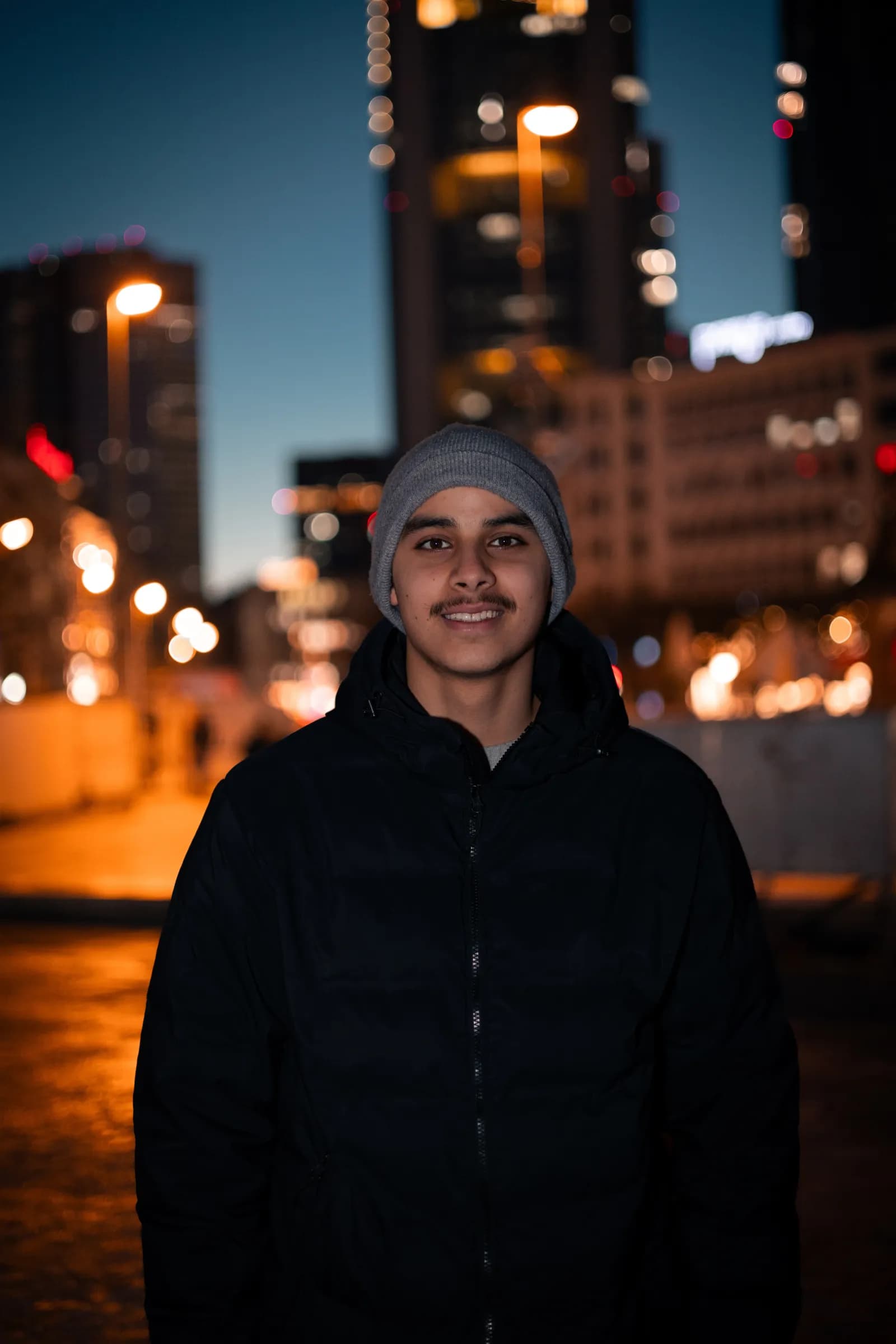 Junger Mann mit Wollmütze bei Nacht – Portrait mit Stadtlichtern im Hintergrund