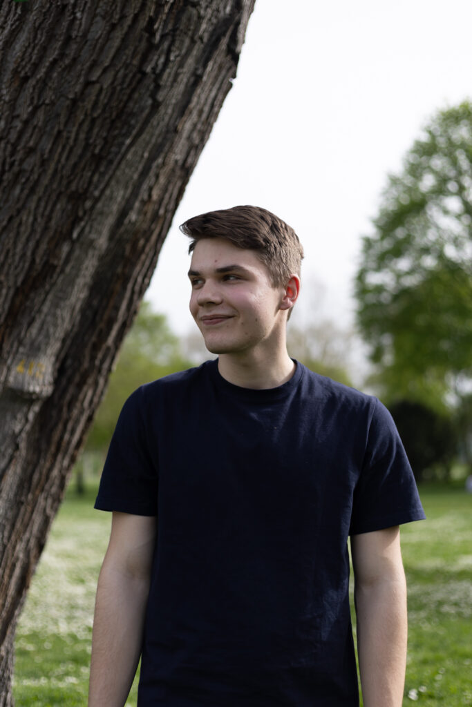 Portrait einer Person im Park neben einem Baum, natürliches Licht und entspannte Outdoor-Szene.