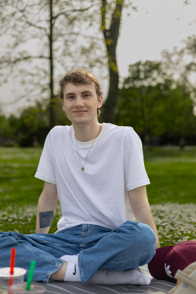 Person sitzt im Park im Gras bei Tageslicht, entspannte Picknick-Atmosphäre.